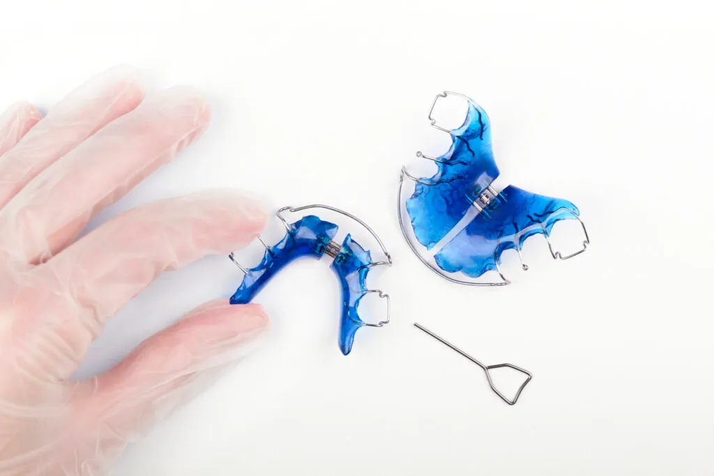 An orthodontists hand with disposable gloves holds Hawley retainers