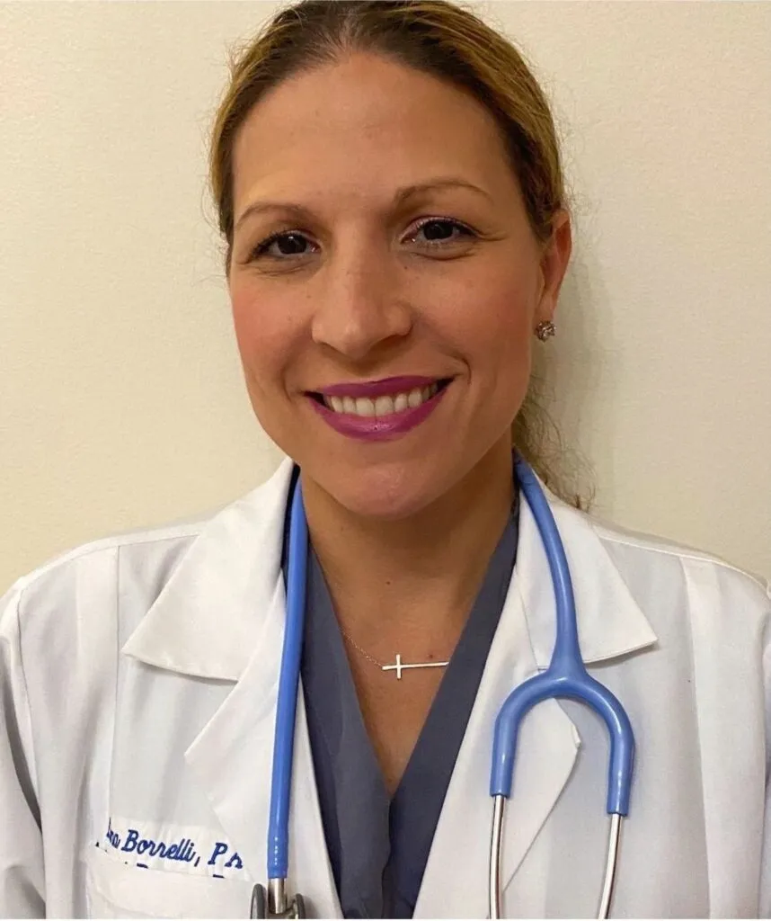A woman wearing a white lab coat and blue stethoscope smiles at the camera.