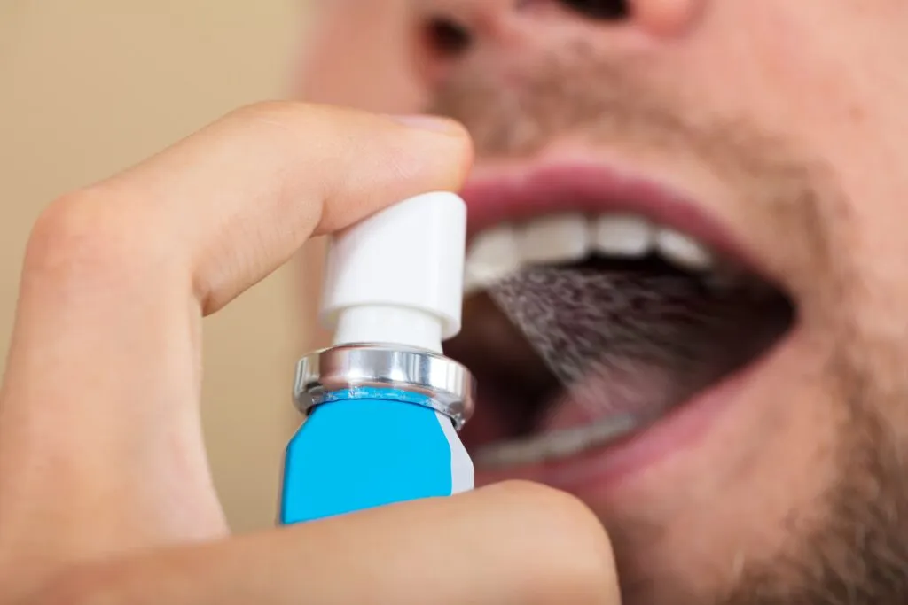 Close up shot of a man spraying his dry mouth with a spray min