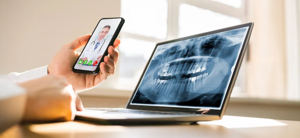 Dentist calling with a patient through video conferencing on mobile as patient views a dental xray result
