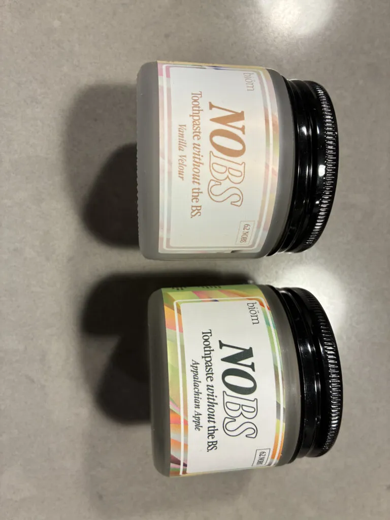 Two jars of NOBS toothpaste tablets, one in Wintergreen flavor and one in Peppermint, are placed on a gray countertop.