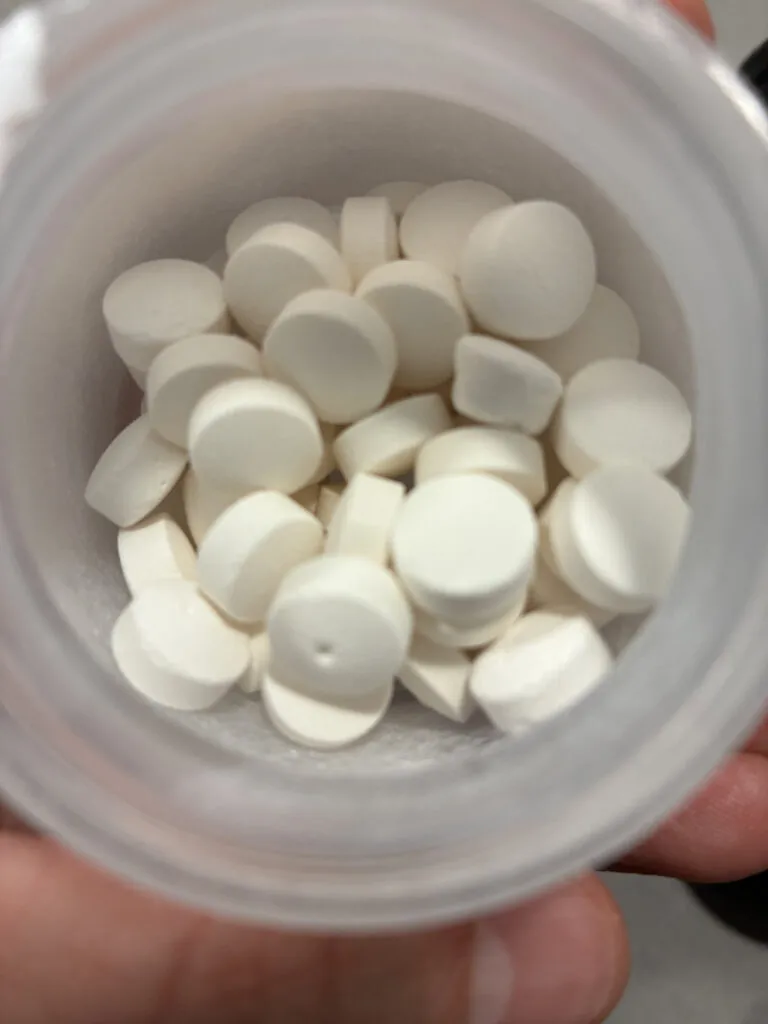 A close-up view of a plastic bottle containing several round, white tablets.