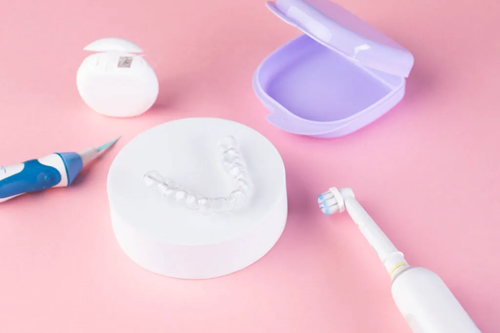 Invisalign clear aligners surrounded by cleaning devices such as electric toothbrush and floss on the table