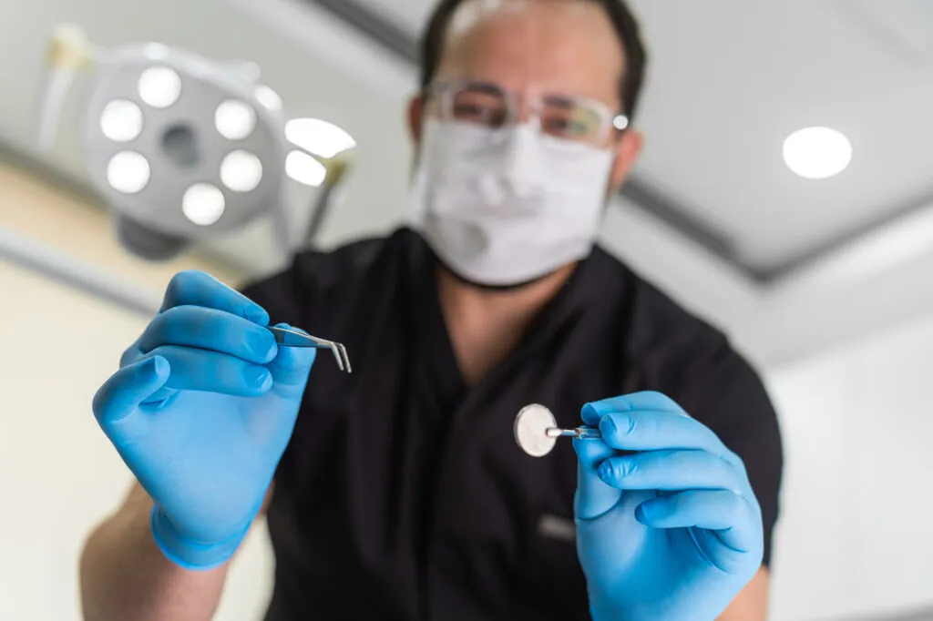 Male dentist in black uniform and gloves reaching to patient POV shot