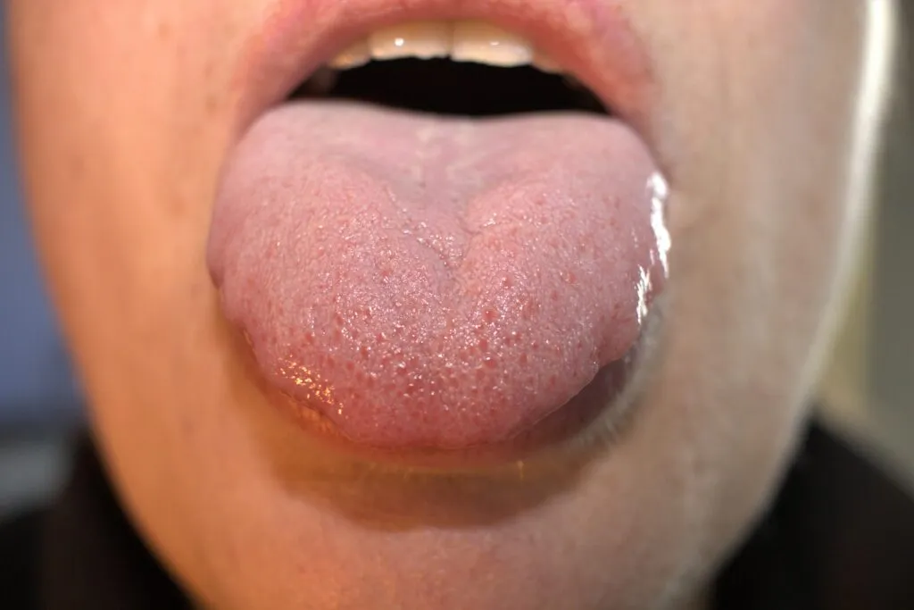 An open mouth with a tongue sticking out, showing the tongue's texture and slight salivation.