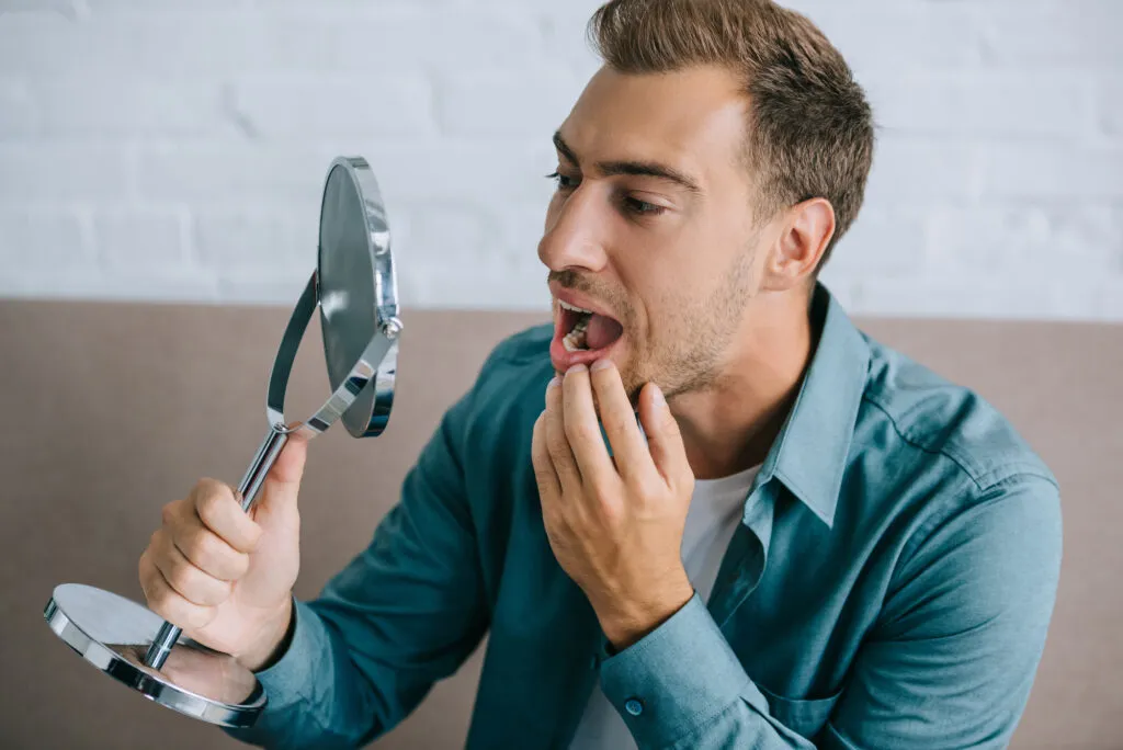 Young man with toothache looking at mirror while sitting at home