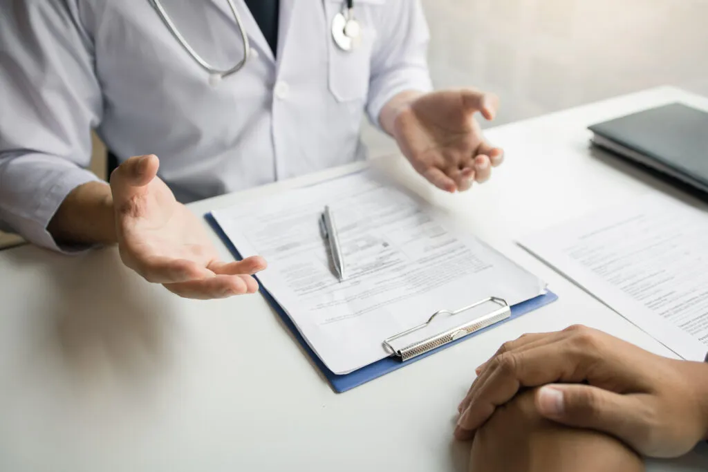 Clipboard on table between doctors two hands