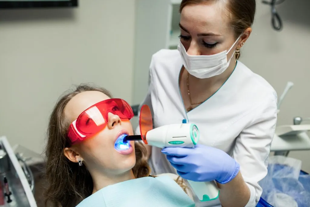 Filling lamp used by dentist assistant on woman patient