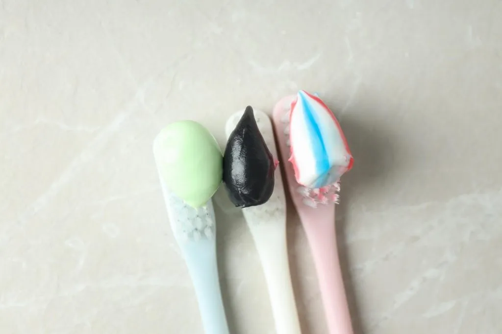 Three different colors of toothpastes on three separate toothbrushes on table