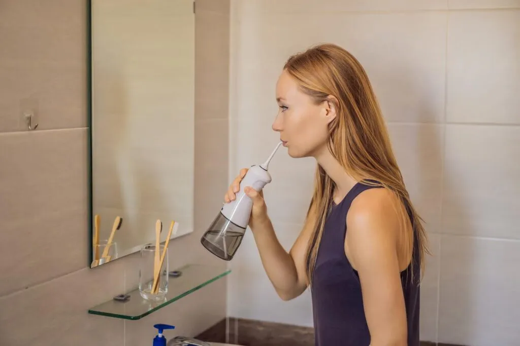 Young woman using oral irrigator in bathroom