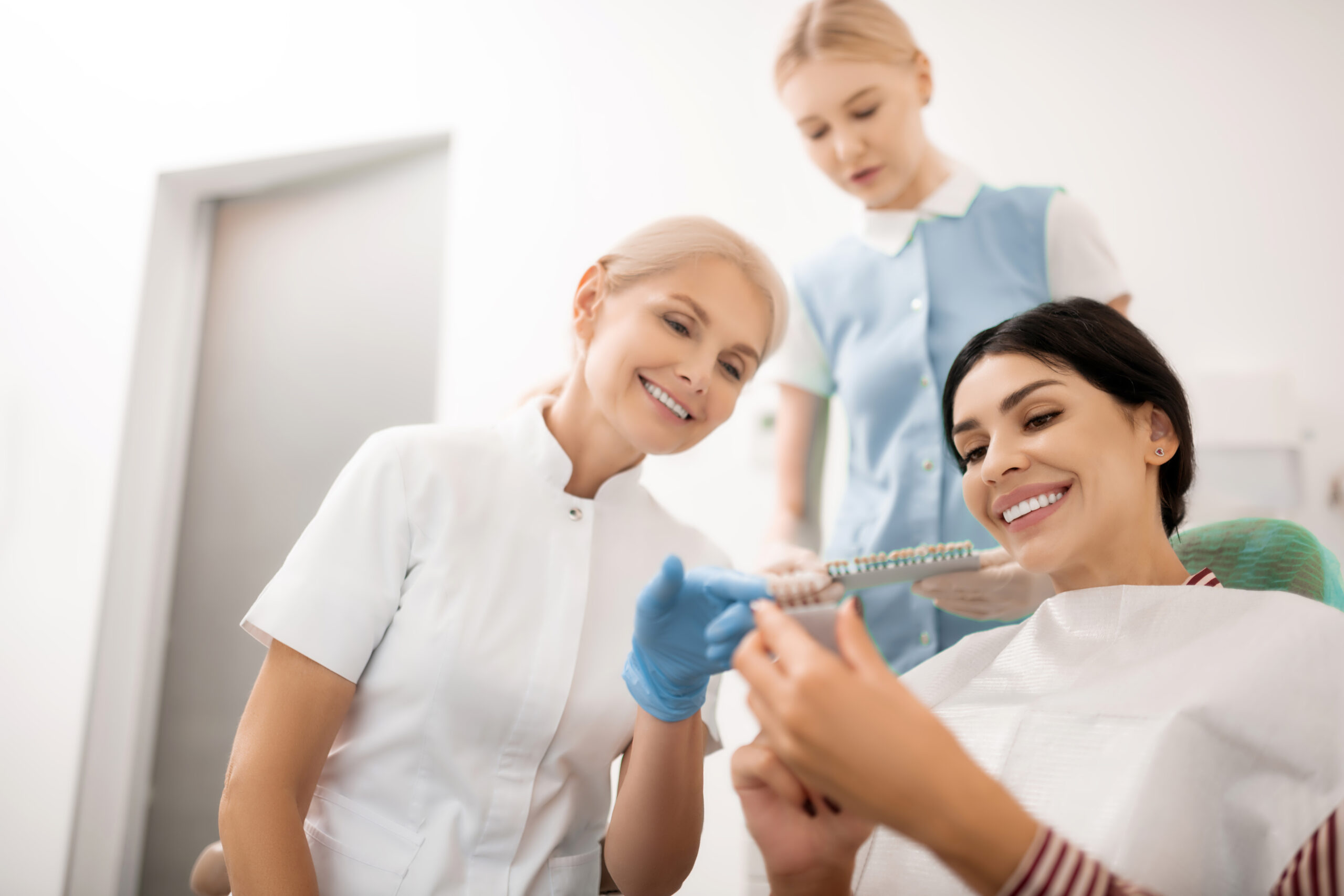 A dentist shows a dental sample to a smiling patient while a dental assistant looks on.