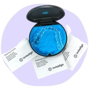 A black case with a blue interior displaying clear aligners surrounded by three packets labeled "Invisalign Cleaning Crystals.